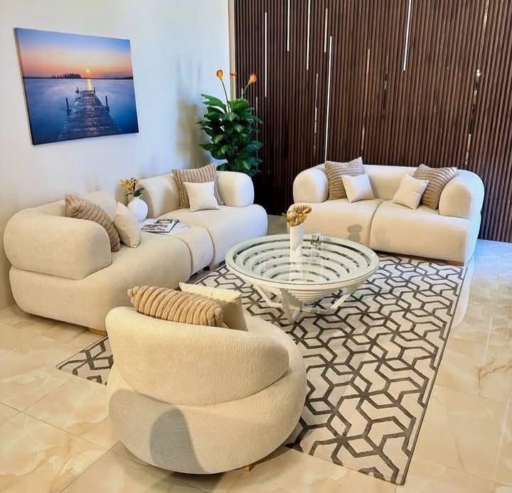 Elegant modern living room with cream curved sofas, geometric rug, and minimalist decor.