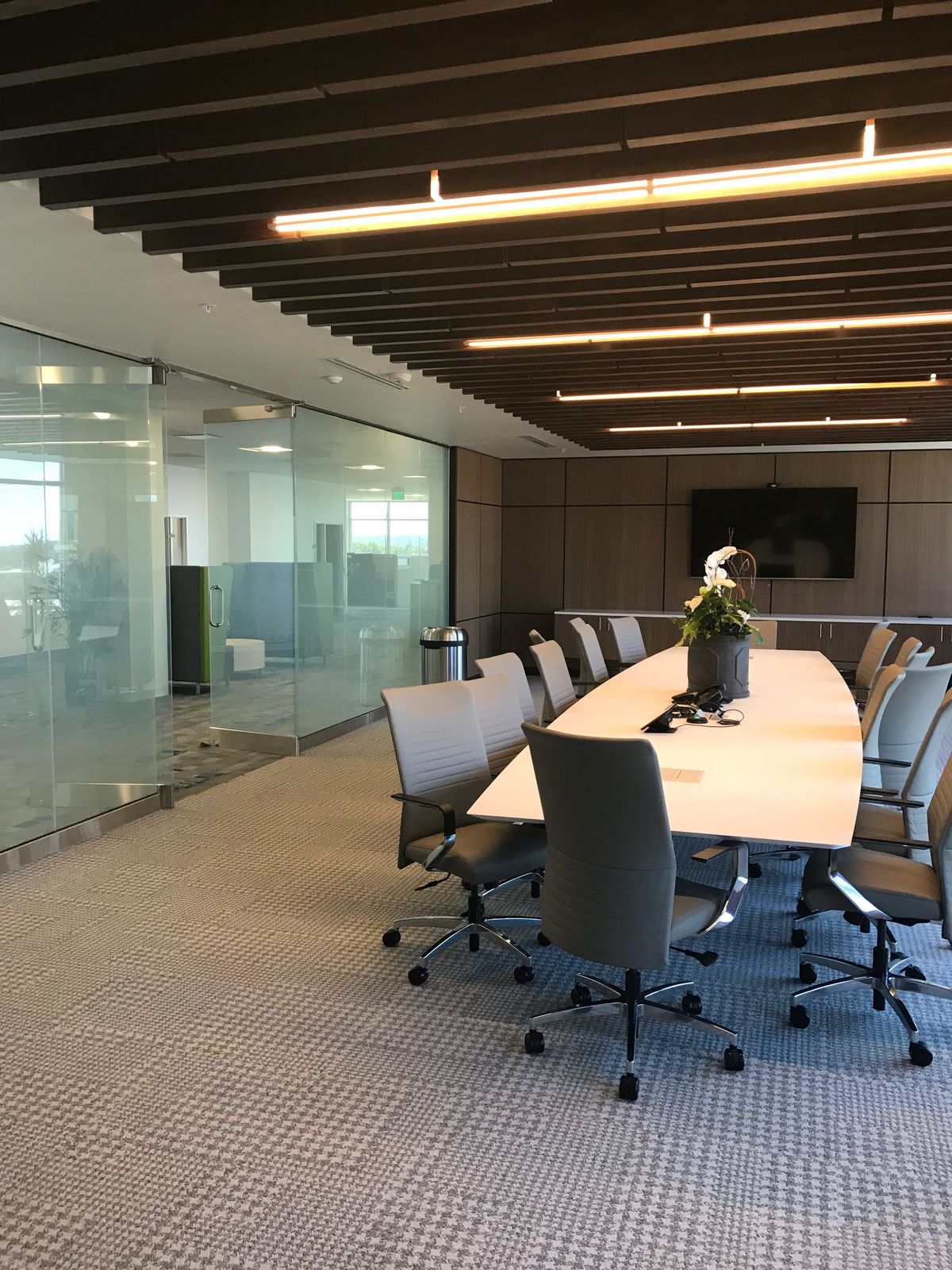 Modern conference room with long wooden table, ergonomic chairs, glass partitions, and professional lighting.